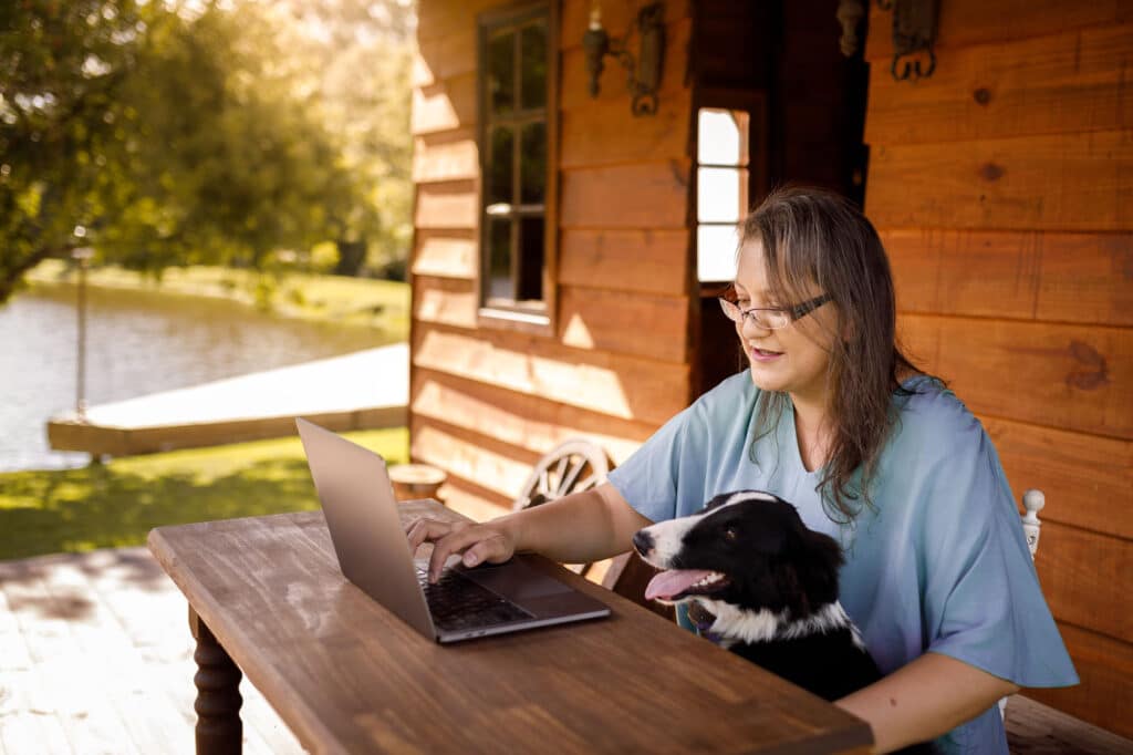 Woman working on laptop at cabin outside with her dog